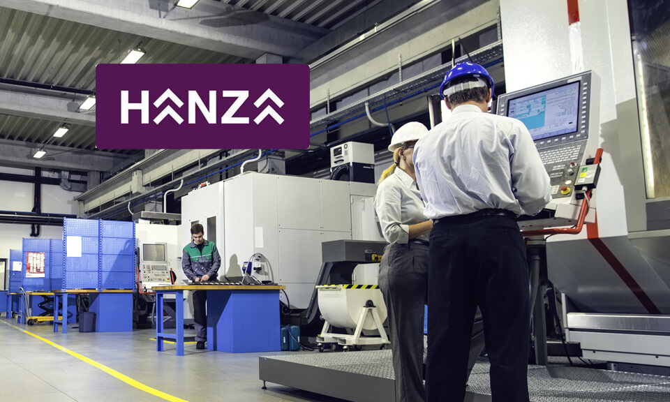 Engineers programming a CNC machine at a manufacturing plant, workers in the background.