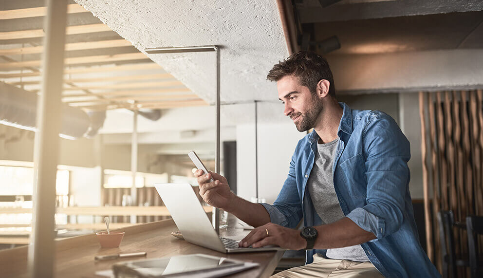 Casually dressed man, showing wireless connectivity by using his laptop and phone at the same time.