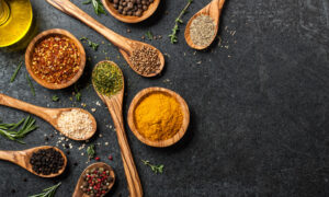 Wooden spoons and bowls holding spices and beans, against a dark grey background