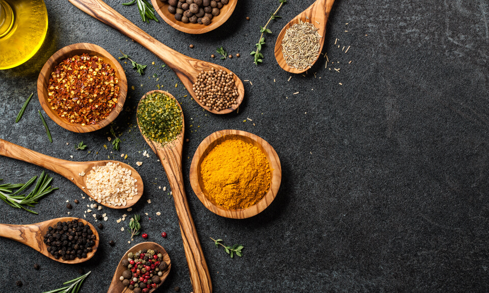 Wooden spoons and bowls holding spices and beans, against a dark grey background