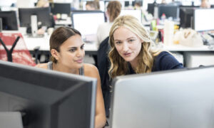 Two female office workers discussing what is on a computer screen