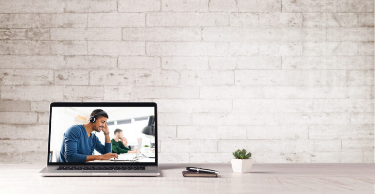 Laptop on a beige table with a pale brick wall behind it