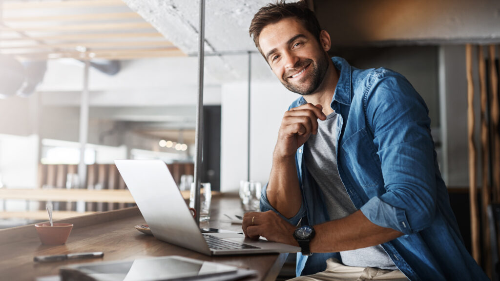 Smiling man in denim shirt using a laptop